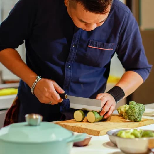 A private chef slicing fresh vegetables in a professional kitchen, representing in-home private chef service.