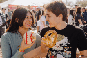 Friends enjoying food at the Innings Festival, holding a baseball-themed treat and a pretzel.