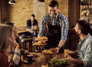 Smiling server delivering burgers and fries to a cheerful group at a restaurant.