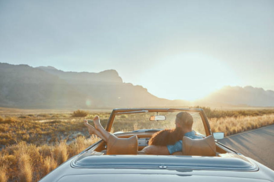 Couple relaxing in a convertible at sunset on a scenic mountain road.