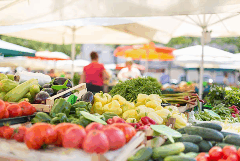 Fresh vegetables displayed at an outdoor farmers market under umbrellas