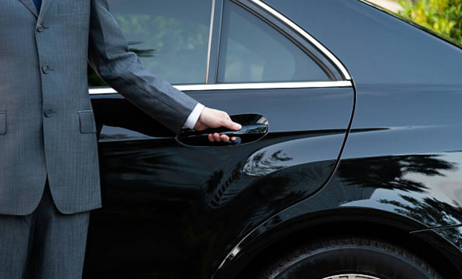 Chauffeur in a suit opening the door of a black luxury car.