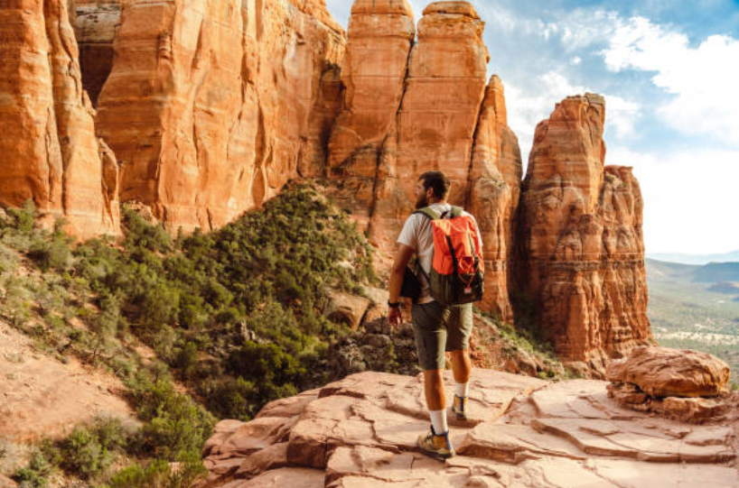 A hiker overlooks sandstone cliffs and a desert valley, highlighting hidden gems in Arizona.