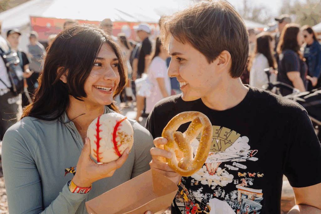 Friends enjoying food at the Innings Festival, holding a baseball-themed treat and a pretzel. 