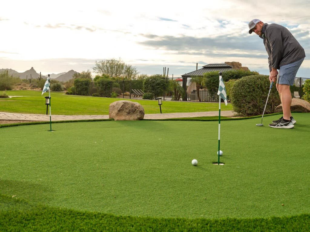 A man putting on a green in the backyard of a luxury meeting space. 