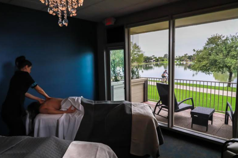 A relaxing massage room at Inspire Day Spa overlooks a serene lake through large sliding glass doors.