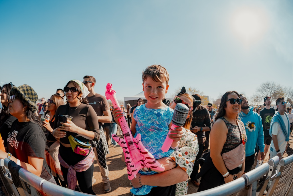 Child holding a toy guitar and microphone in a festival crowd